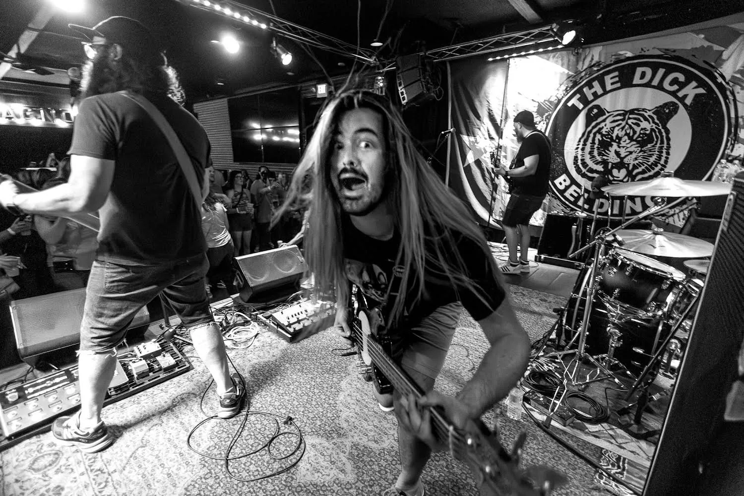 A wide-angle black-and-white shot from behind The Dick Beldings’ drum kit